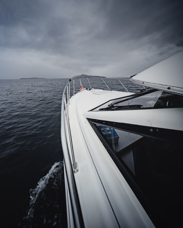 a grey photo of a power boat heading straight into the clouds on the horizon of the ocean.