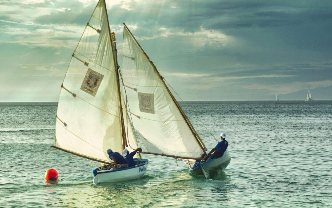 Two sailboats bump into one another at the water during cloudy weather.