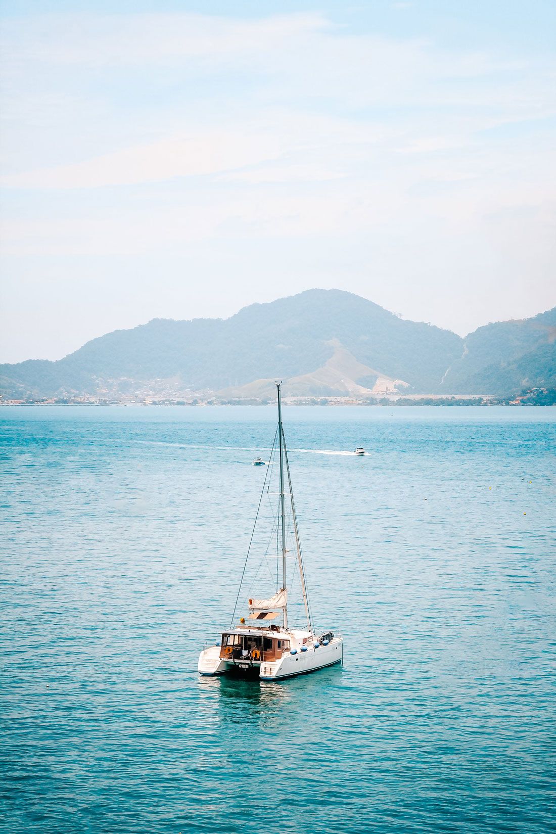 a sailboat on the ocean, mountains in the back.