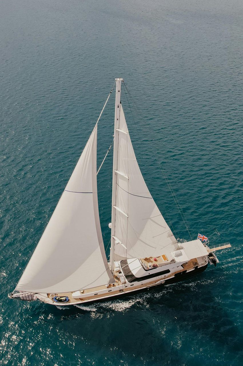 A top-down image of a powerboat being driven along blue seas. There is someone wakeboarding behind the boat.