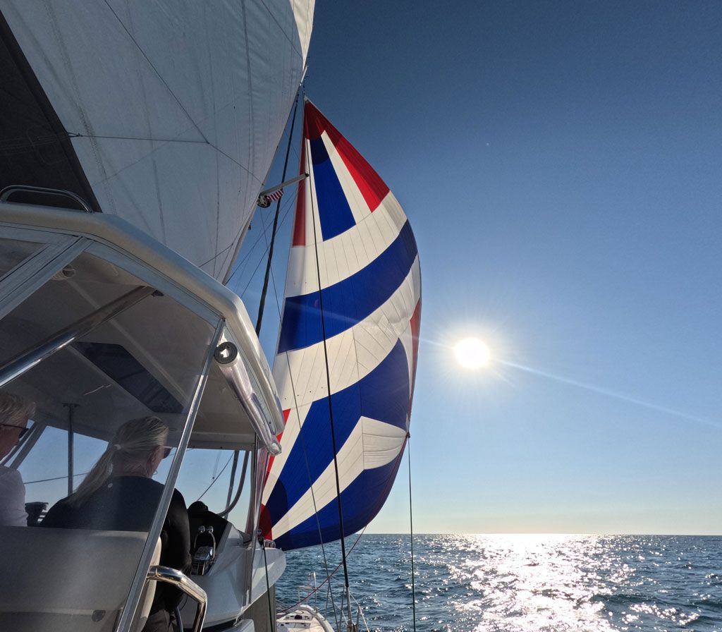 Sailboats near the shore of the ocean, which is a bright blue. The sky is blue with a few white clouds.